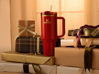 Stanley 1913 red Quencher tumbler with straw and handle, surrounded by holiday gift boxes with ribbons.