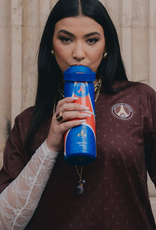 Stanley 1913 AeroLight water bottle in PSG blue, held by a woman in Paris Saint-Germain jersey, drinking from it.