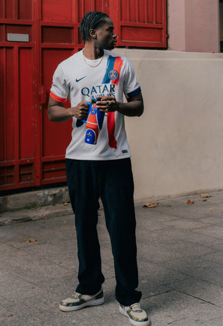 Stanley 1913 bottle held by man in PSG white Nike jersey, standing on urban street near red doors.