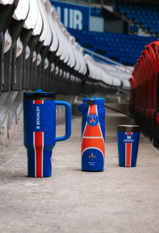 Stanley 1913 x PSG blue and red drinkware set — tumbler, Aerolight bottle, and cup — displayed in a stadium.